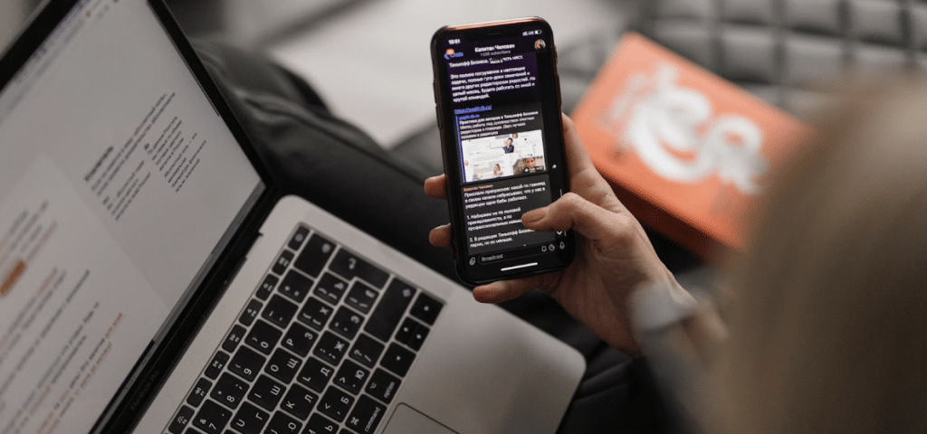 Young caucasian woman on leather couch working at a laptop while browsing her phone